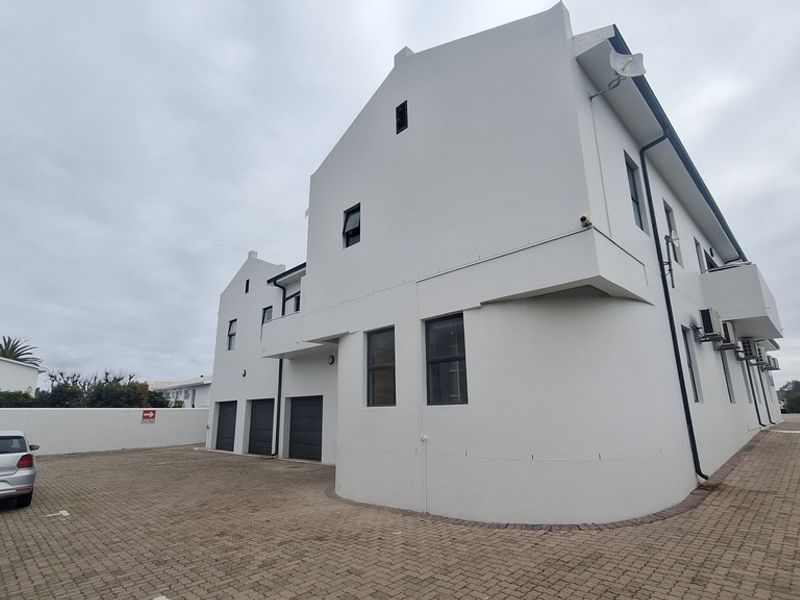 Exterior view of a modern apartment building featuring a paved driveway, multiple garage access points, and white rendered facade.