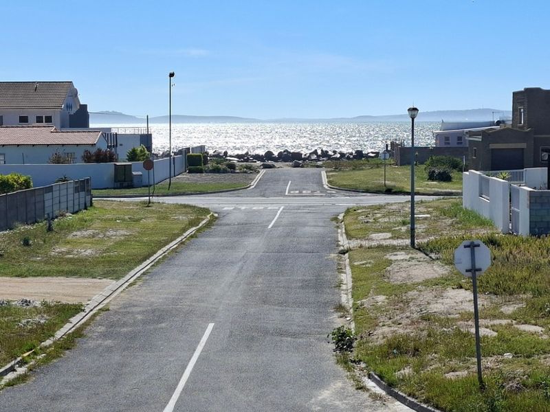 A street view looking down a residential road towards the ocean, showcasing the coastal neighborhood setting and proximity to the beach.