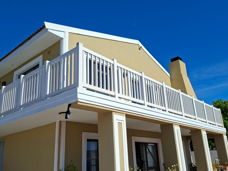 A well-maintained exterior view of the property featuring a spacious upper-level balcony with white balustrades and a prominent chimney stack.