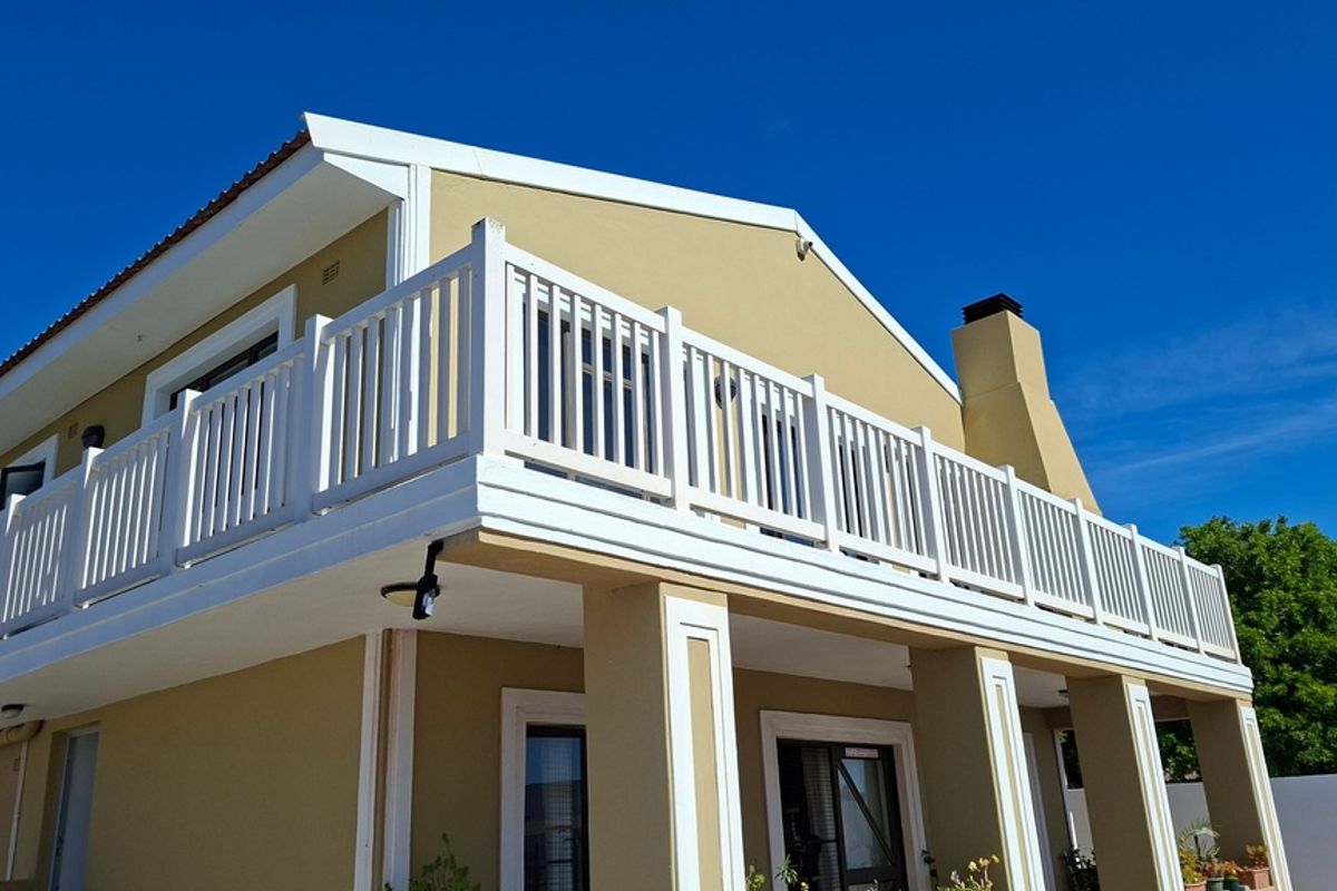 A well-maintained exterior view of the property featuring a spacious upper-level balcony with white balustrades and a prominent chimney stack.