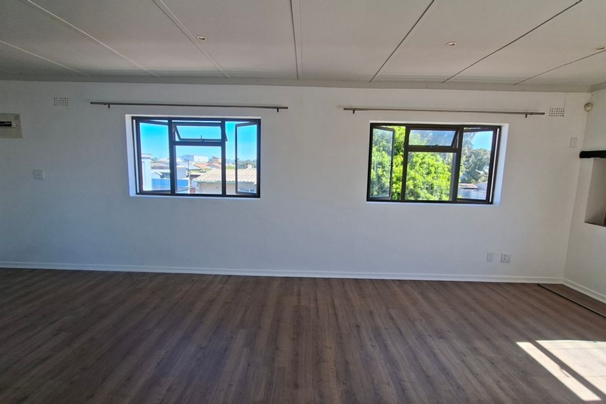 A bright, empty living room featuring modern laminate flooring, recessed ceiling lighting, and dual casement windows providing natural light.
