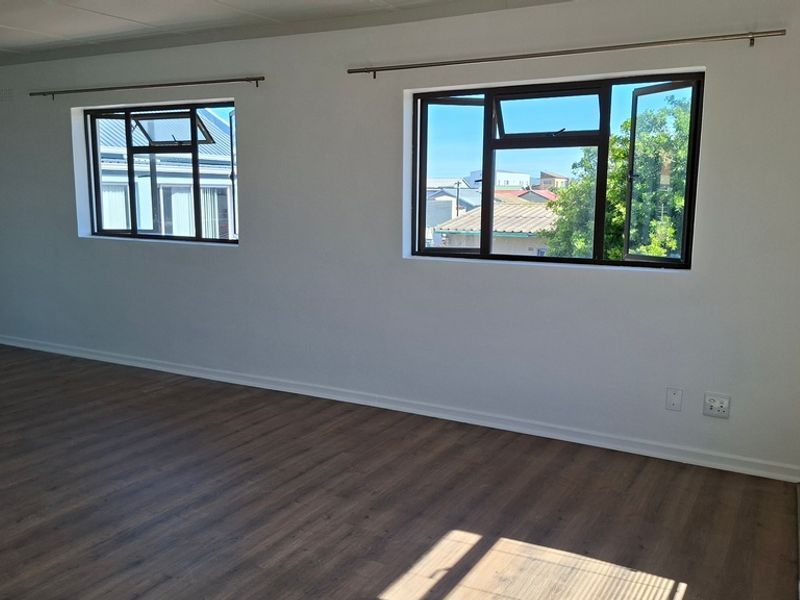A bright, empty living area featuring modern laminate flooring, neutral walls, and aluminium-framed windows with curtain rods installed.