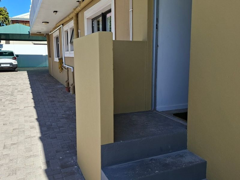 Exterior view of the apartment entrance featuring concrete steps and a paved driveway area with external wall lighting.