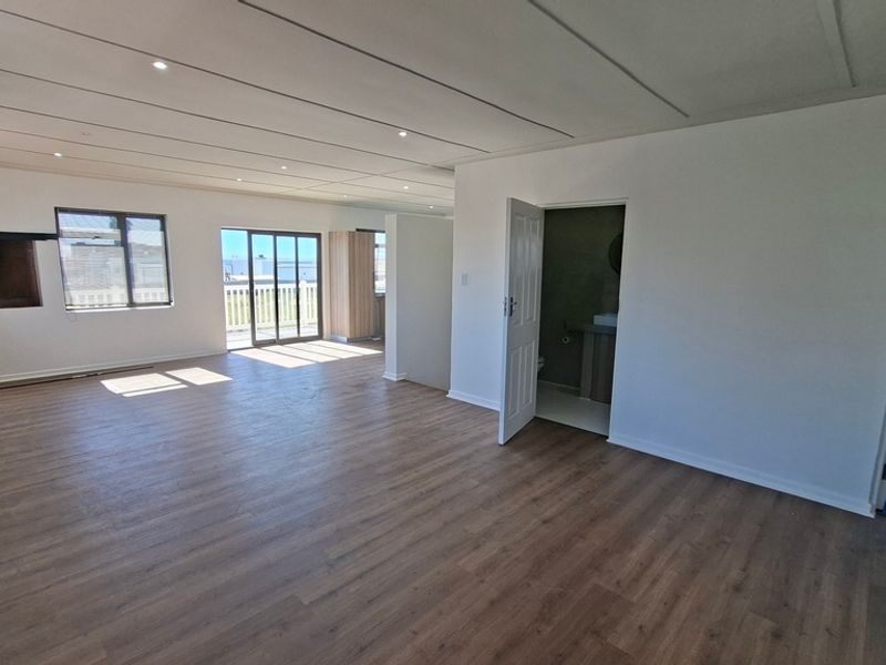 Spacious open-plan living area featuring modern laminate flooring, recessed lighting, and a built-in fireplace, with direct access to an outdoor balcony.