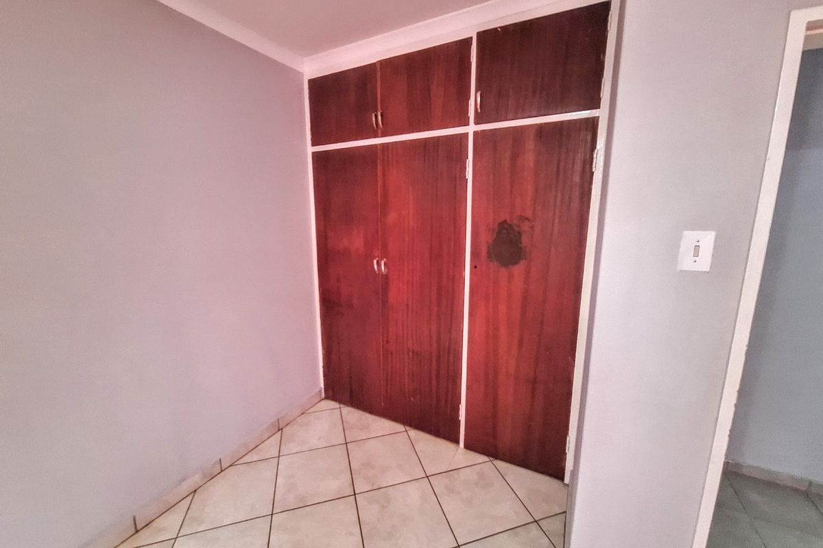 A vacant bedroom featuring tiled flooring and built-in wooden cupboards with visible surface wear.