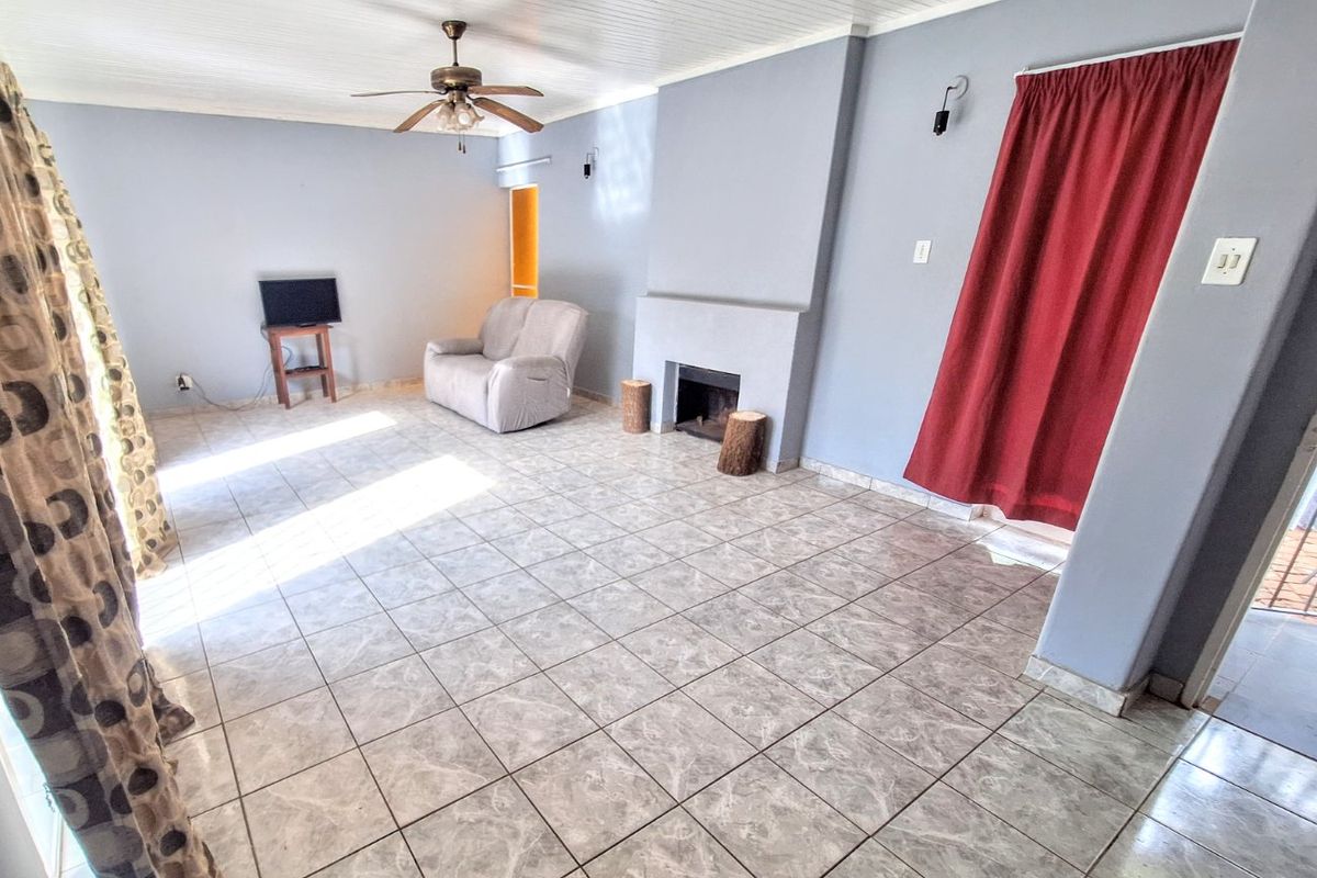 Spacious living room featuring tiled flooring, a built-in fireplace, and a ceiling fan, offering a functional layout with neutral wall finishes.