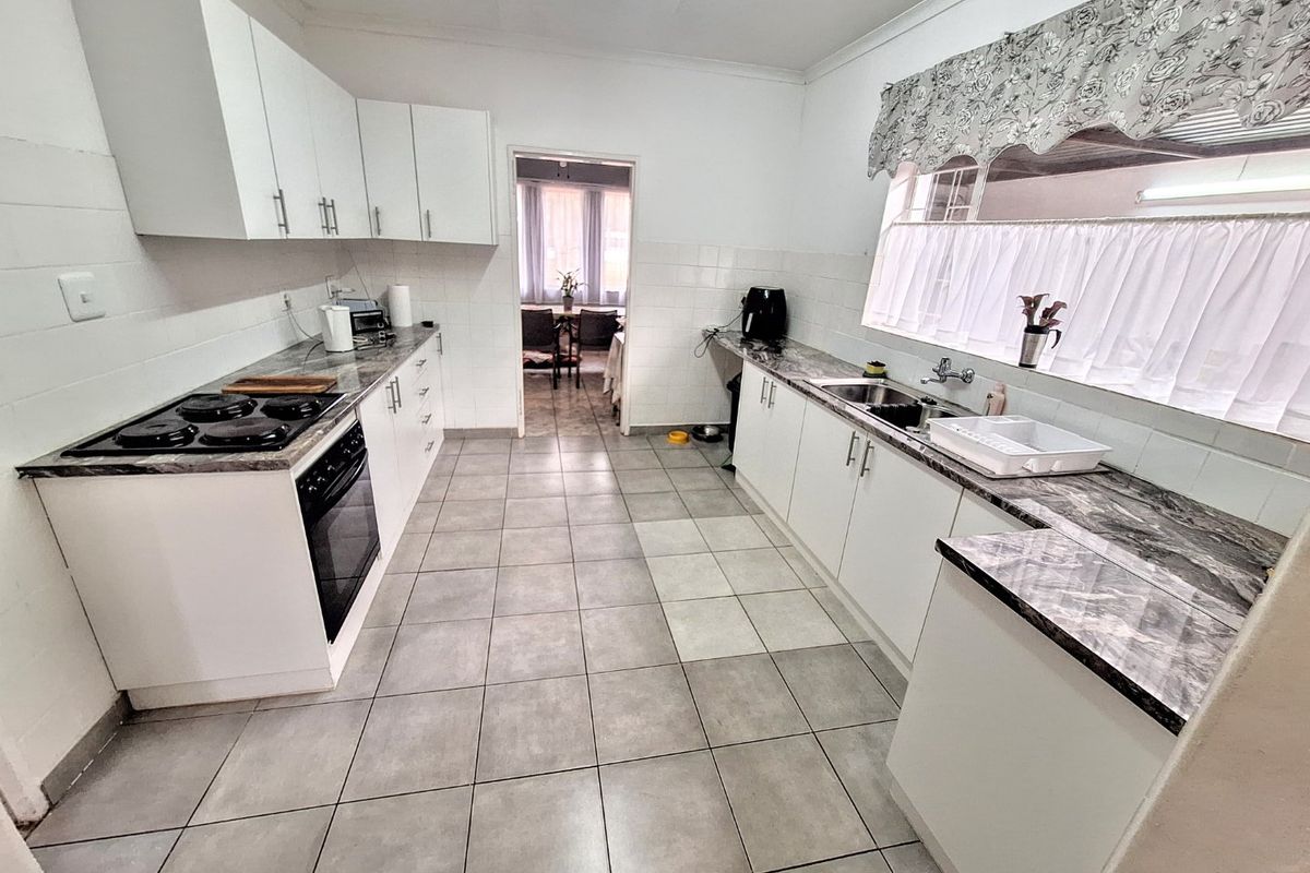 A functional kitchen featuring white cabinetry, marble-look laminate countertops, an electric hob, built-in oven, and tiled flooring with a neutral aesthetic.