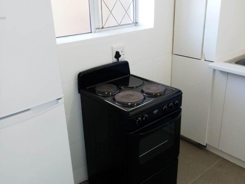 A functional kitchen area featuring a freestanding electric stove, tiled flooring, and built-in cabinetry with a window providing natural light.