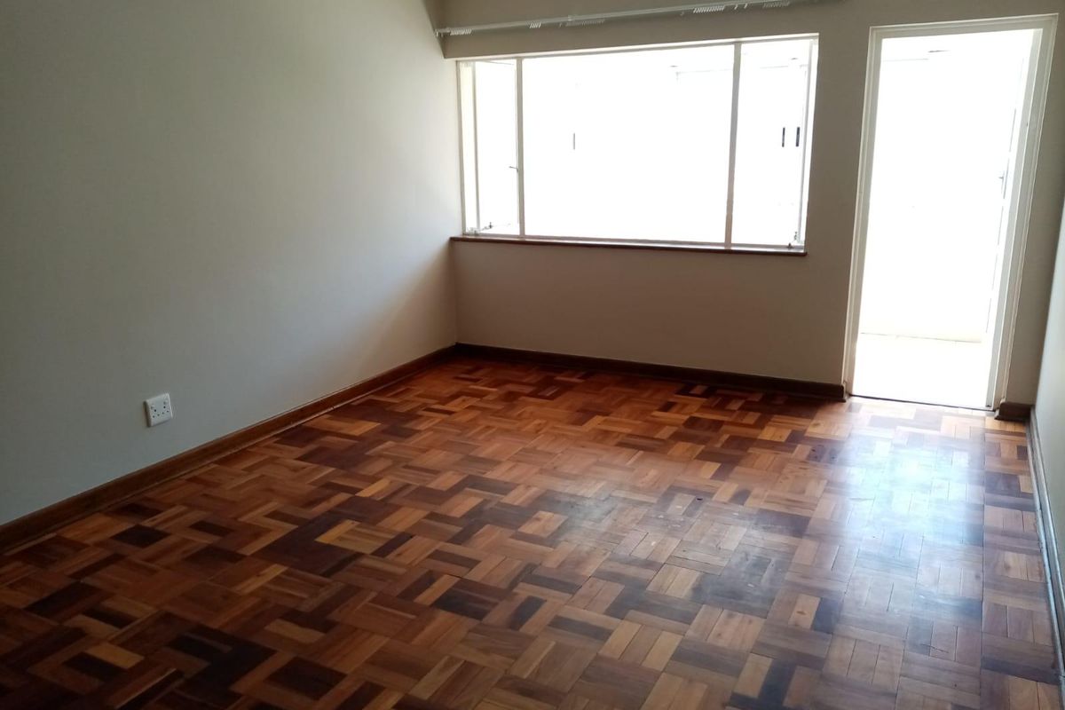 An empty bedroom featuring classic parquet flooring, neutral walls, and natural light from a large window and adjacent door.