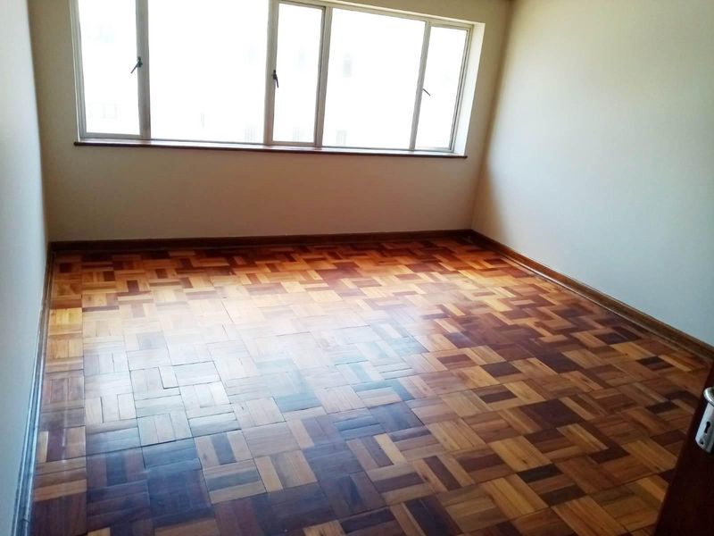 An empty bedroom featuring traditional parquet flooring and large windows, providing a blank canvas for interior design and renovation.