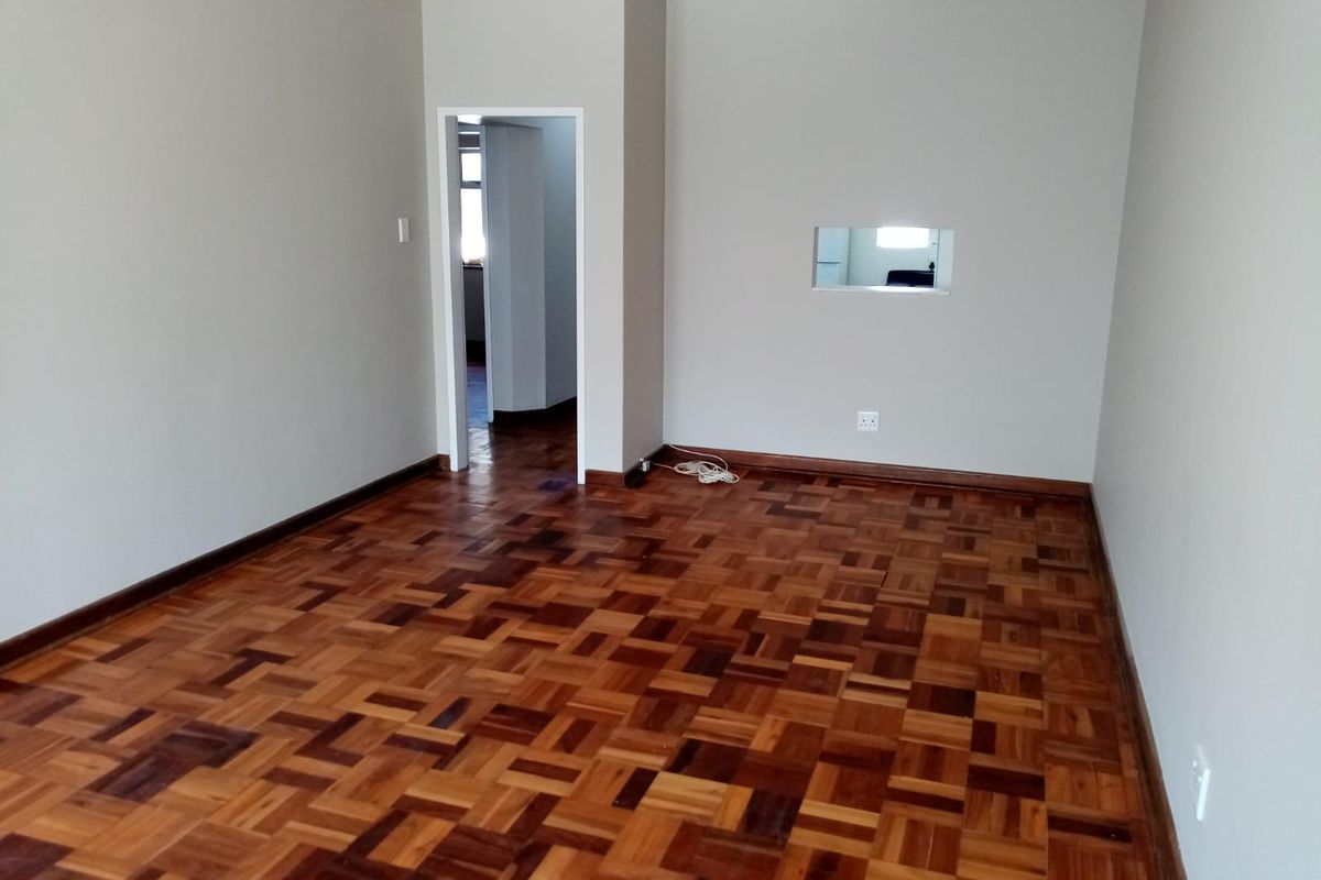 An empty living room featuring classic parquet flooring, neutral walls, and a convenient pass-through window connecting to the adjacent space.