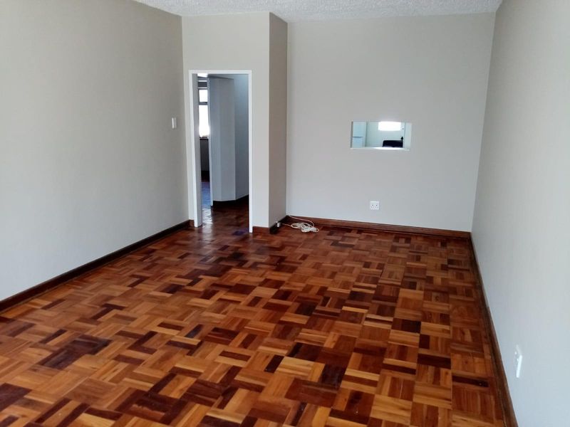 An empty living room featuring classic parquet flooring, neutral walls, and a convenient pass-through window connecting to the adjacent space.