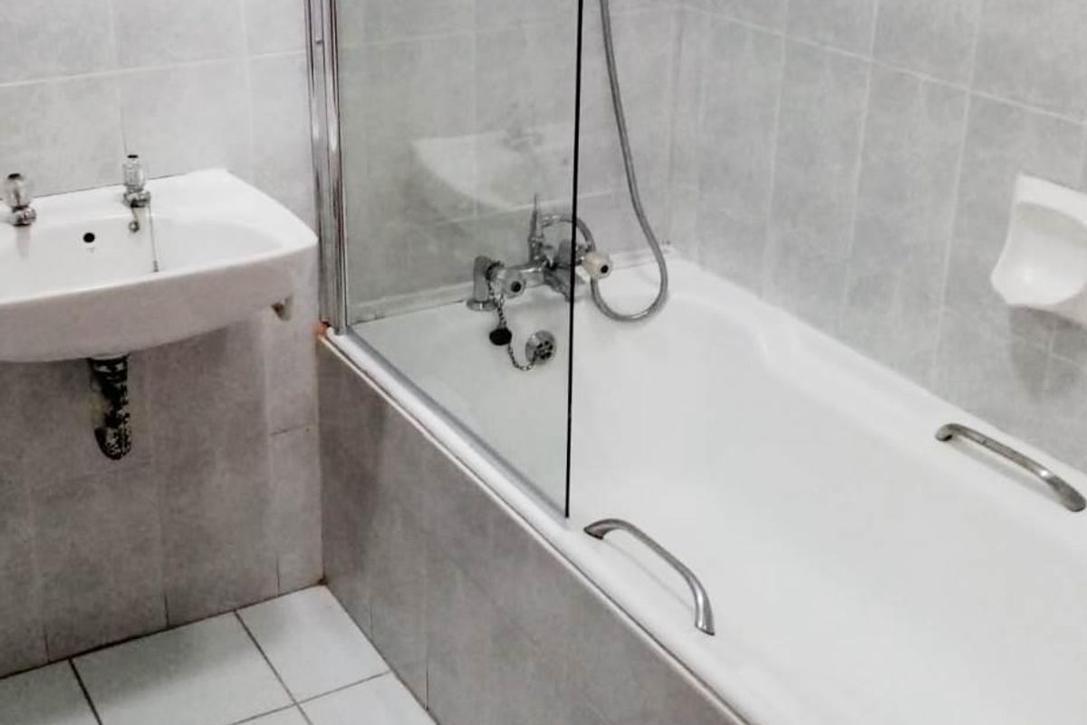A functional bathroom featuring a wall-mounted basin, a bathtub with a glass shower screen, and neutral ceramic tiling throughout.