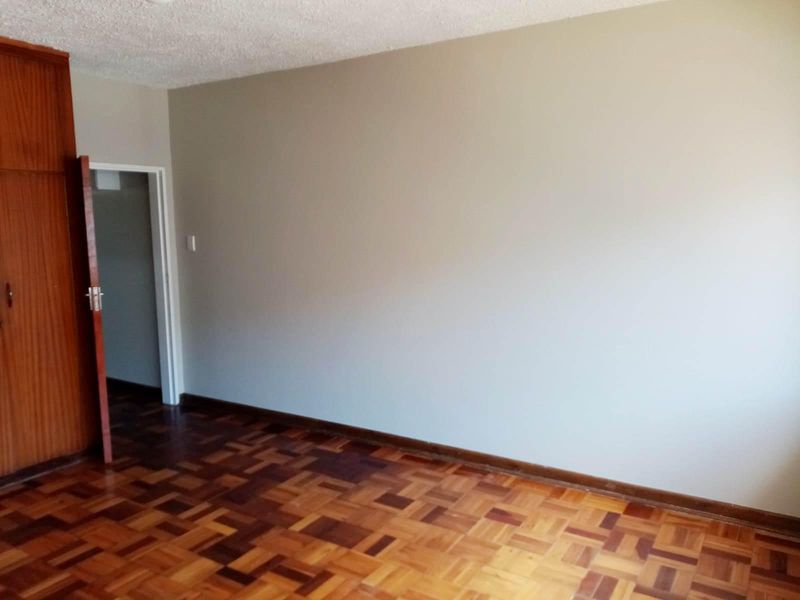 An empty bedroom featuring classic parquet flooring and a built-in wooden wardrobe, offering a neutral canvas for interior design updates.