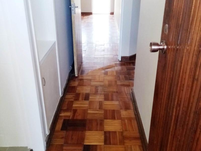 A bright hallway featuring classic parquet flooring and a built-in storage cupboard, leading through to an adjacent room.