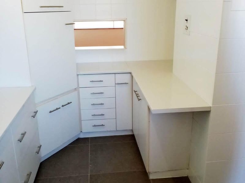 A clean, modern kitchen area featuring white built-in cabinetry, ample countertop space, and neutral tiled flooring, offering a functional and bright workspace.