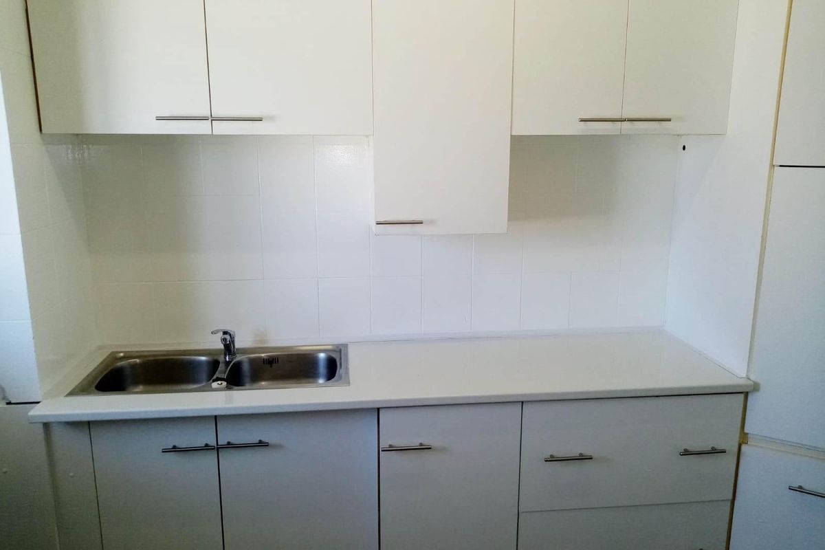 A clean, functional kitchen featuring white cabinetry, a double bowl stainless steel sink, and a tiled splashback.