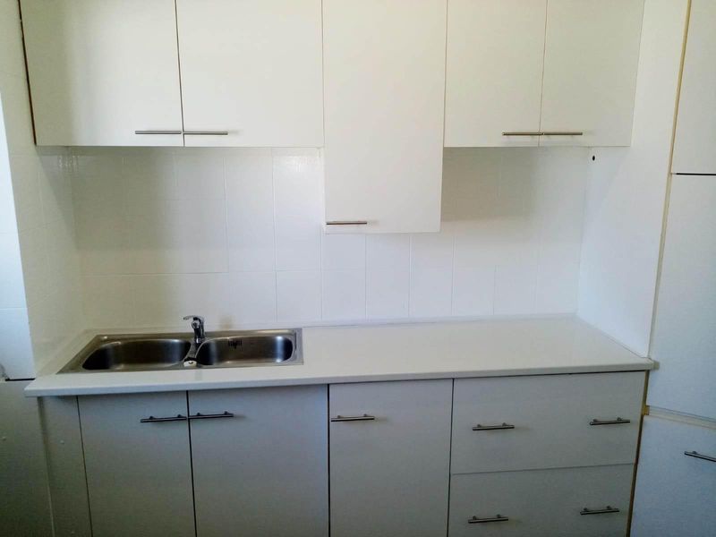 A clean, functional kitchen featuring white cabinetry, a double bowl stainless steel sink, and a tiled splashback.