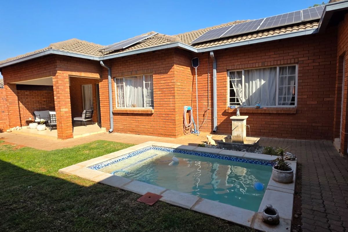 Rear exterior view of a brick townhouse featuring a private swimming pool, covered patio area, and roof-mounted solar panels.