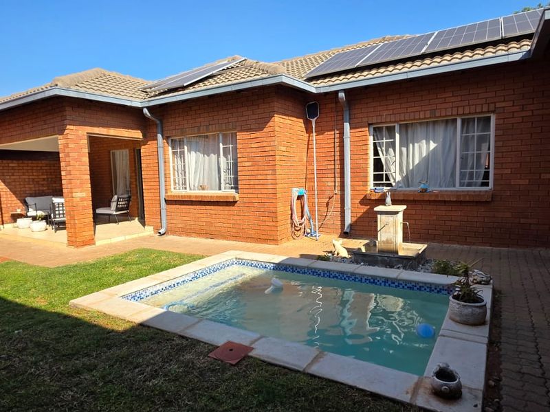 Rear exterior view of a brick townhouse featuring a private swimming pool, covered patio area, and roof-mounted solar panels.