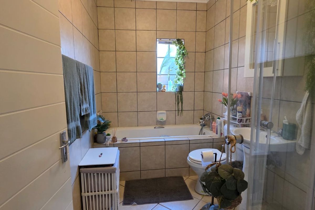 A functional bathroom featuring a bathtub, separate shower enclosure, pedestal basin, and toilet with neutral wall and floor tiling.
