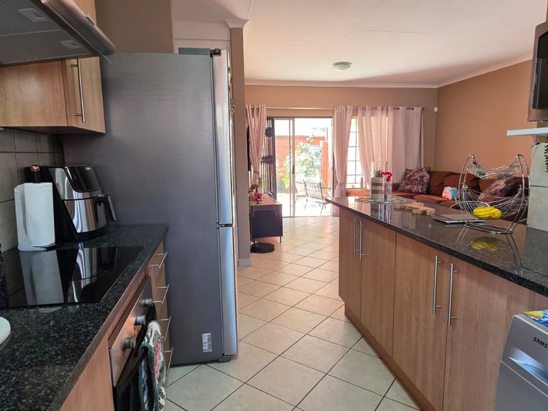 Open-plan kitchen and living area featuring granite countertops, wood-finish cabinetry, and ceramic tile flooring, leading out to a patio through sliding glass doors.