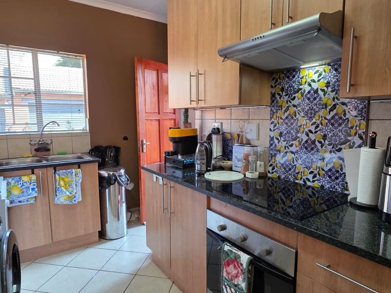 A functional kitchen featuring wood-finish cabinetry, granite countertops, a decorative backsplash, and integrated appliances including an oven, hob, and extractor fan.