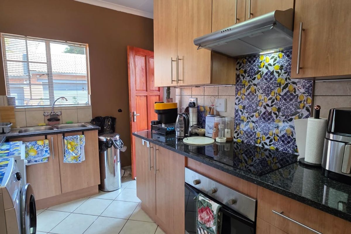 A functional kitchen featuring wood-finish cabinetry, granite countertops, a decorative backsplash, and integrated appliances including an oven, hob, and extractor fan.