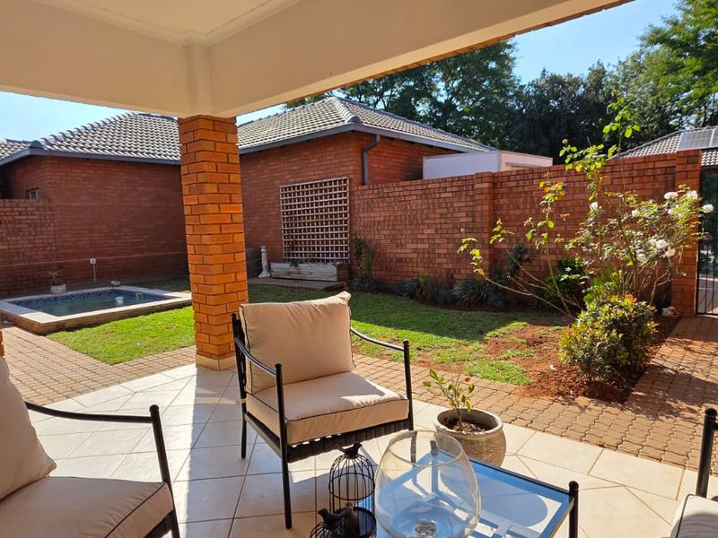 A covered patio overlooking a private garden with a small plunge pool, brick boundary walls, and paved pathways.