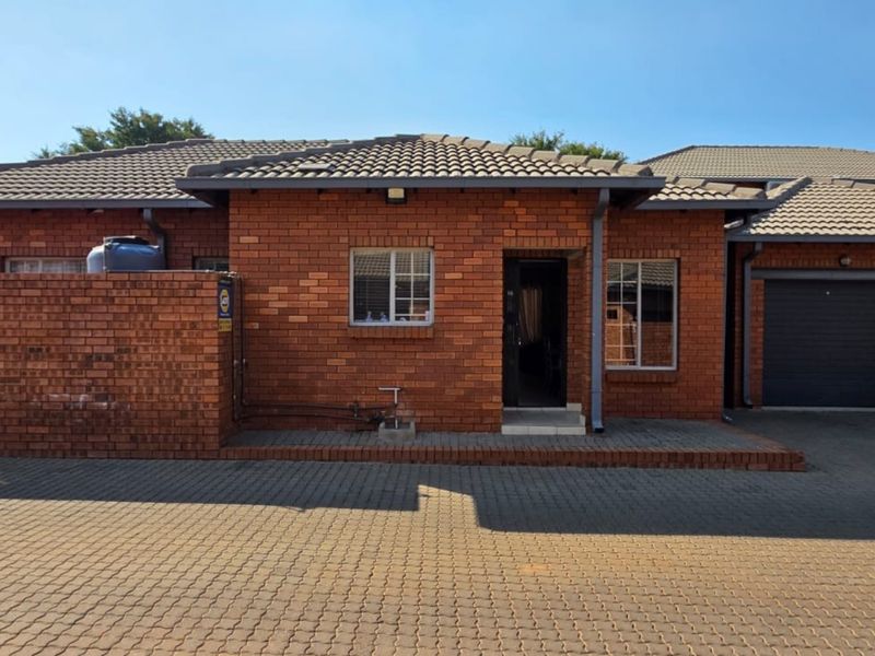 Front elevation of a face brick townhouse featuring a double garage, paved driveway, and a private boundary wall.