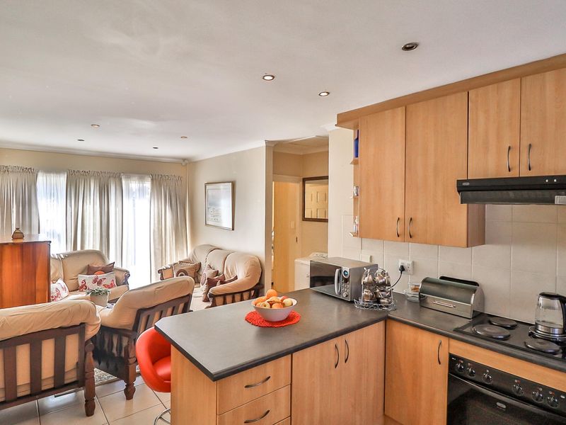 Open-plan living area featuring a functional kitchen with wood-finish cabinetry, electric hob, and oven, flowing into a comfortable lounge space with tiled floors.