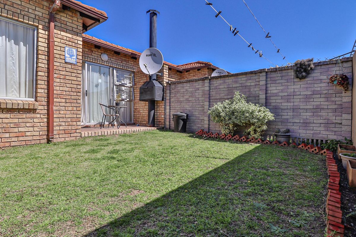 A private rear garden featuring a brick boundary wall, a built-in braai, and direct access to the home via a sliding glass door.