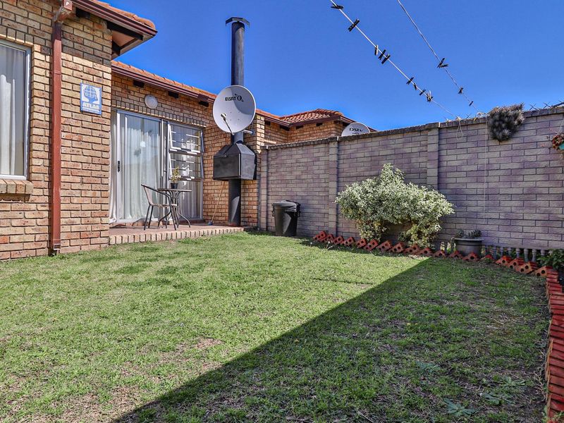 A private rear garden featuring a brick boundary wall, a built-in braai, and direct access to the home via a sliding glass door.