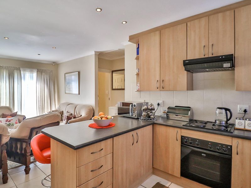 Open-plan kitchen and living area featuring light wood cabinetry, dark countertops, built-in cooking appliances, and tiled flooring throughout.