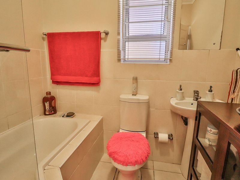 A functional bathroom featuring a bathtub, pedestal sink, and toilet with neutral wall tiling and a window with blinds.