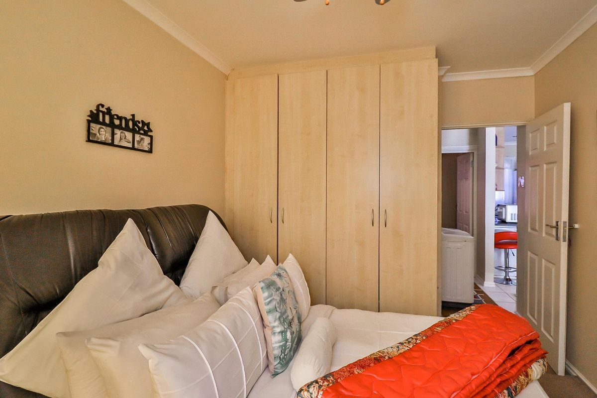 A bedroom featuring light wood-finish built-in cupboards and coving, with an adjacent view into a kitchen area.