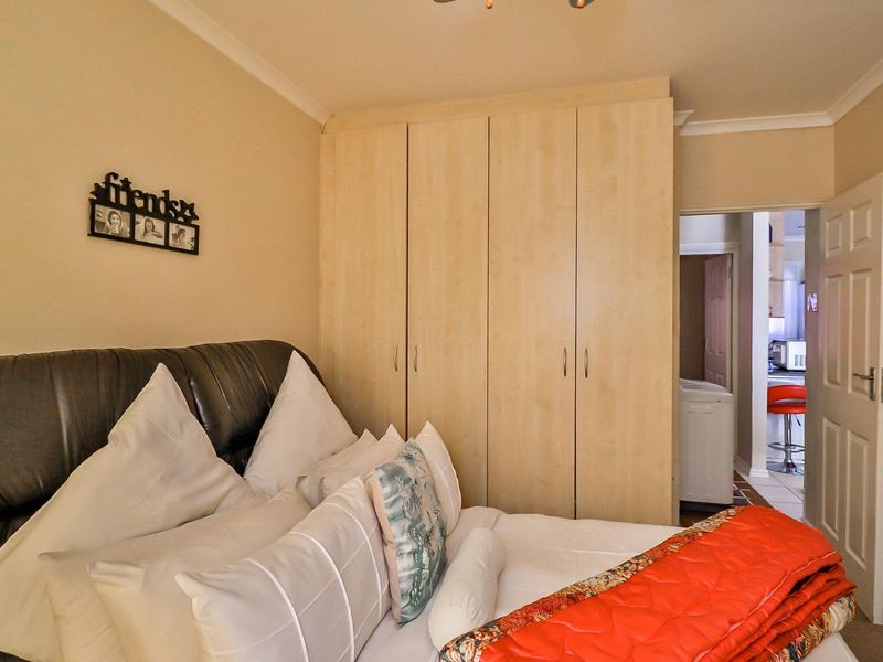A bedroom featuring light wood-finish built-in cupboards and coving, with an adjacent view into a kitchen area.