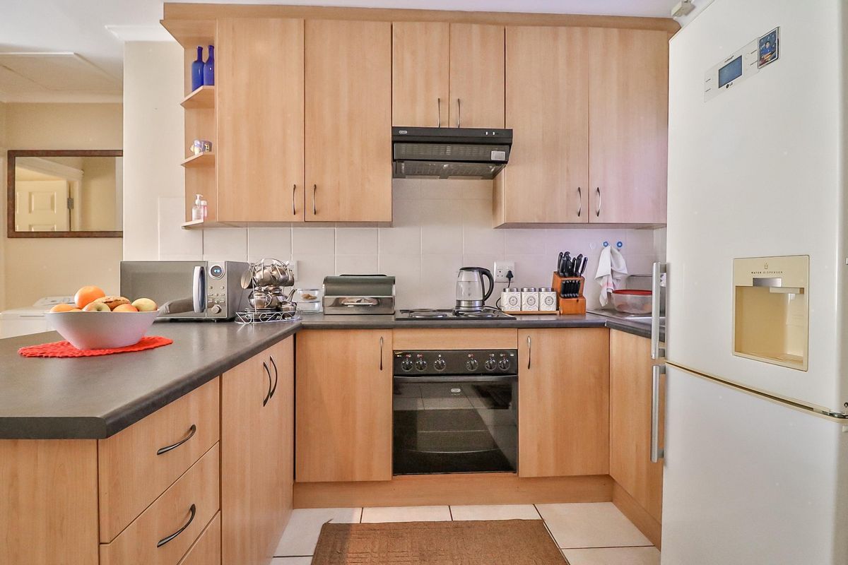 A functional kitchen featuring light wood-finish cabinetry, dark laminate countertops, built-in oven, electric hob, and a tiled backsplash.