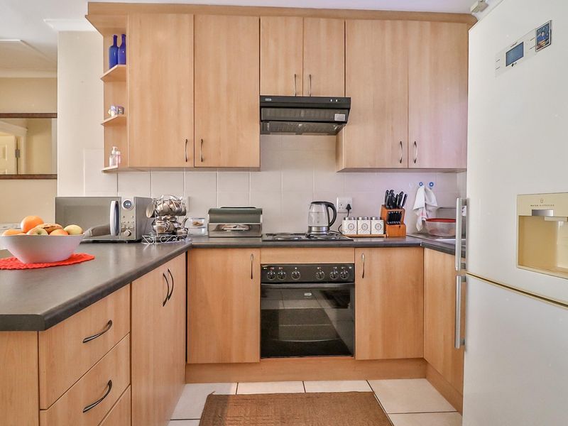 A functional kitchen featuring light wood-finish cabinetry, dark laminate countertops, built-in oven, electric hob, and a tiled backsplash.