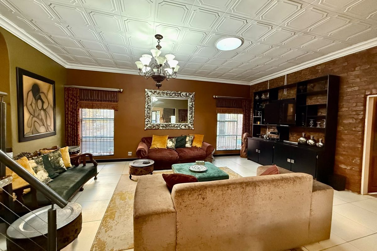 Spacious living room featuring a decorative coffered ceiling, exposed brick accent wall, tiled flooring, and a built-in shelving unit.