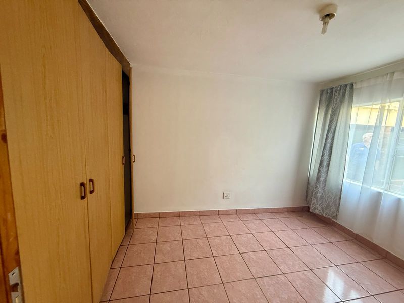 A vacant bedroom featuring built-in wooden cupboards and tiled flooring, offering a blank canvas for potential updates.