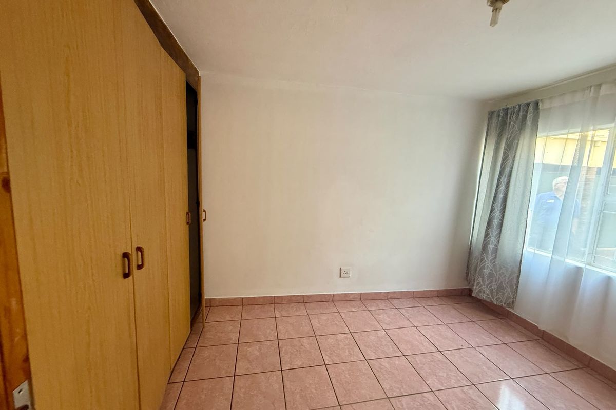A vacant bedroom featuring built-in wooden cupboards and tiled flooring, offering a blank canvas for potential updates.
