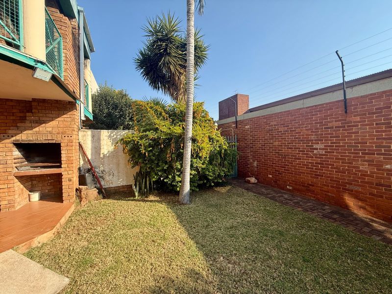 Private rear garden featuring a built-in braai area, brick boundary walls with electric fencing, and a small lawn.