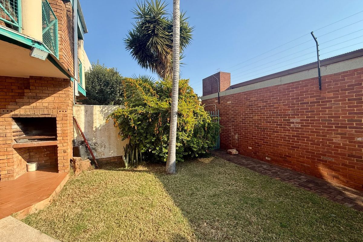 Private rear garden featuring a built-in braai area, brick boundary walls with electric fencing, and a small lawn.