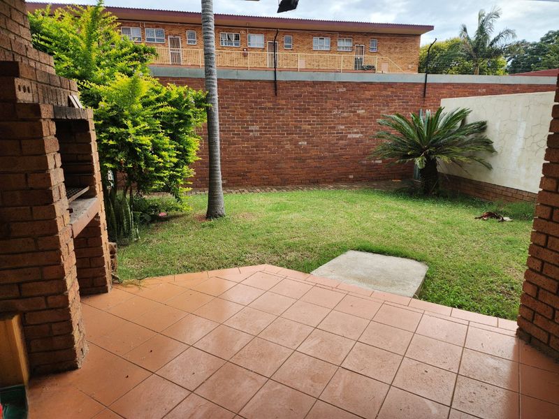 A private outdoor patio area featuring a built-in brick braai, tiled flooring, and a small garden space enclosed by a brick boundary wall.
