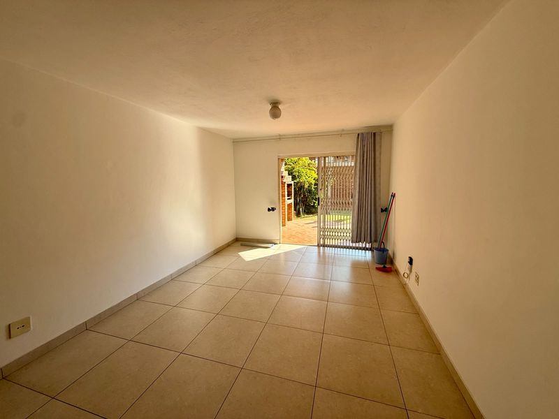 An empty, neutrally painted living room featuring tiled flooring and a sliding glass door providing access to an outdoor patio area.