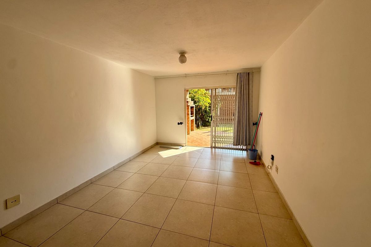 An empty, neutrally painted living room featuring tiled flooring and a sliding glass door providing access to an outdoor patio area.