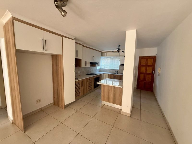 A clean, modern kitchen featuring light wood-tone cabinetry, integrated appliances, tiled flooring, and a functional breakfast nook layout.