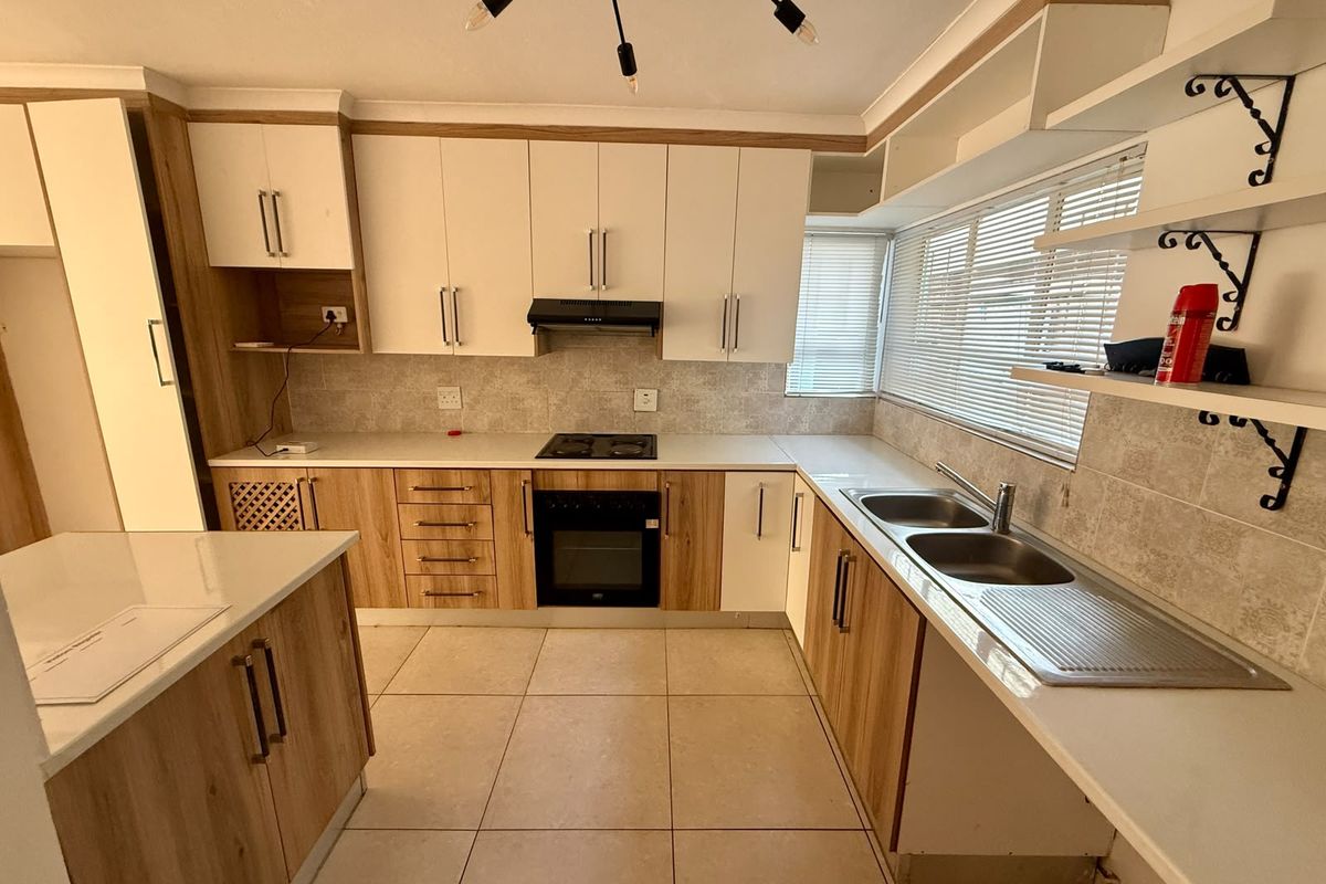 A functional kitchen featuring wood-look and white cabinetry, a built-in oven with hob, a kitchen island, and tiled flooring.