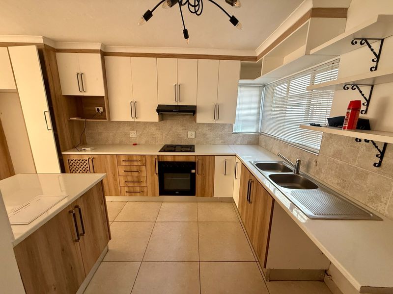 A functional kitchen featuring wood-look and white cabinetry, a built-in oven with hob, a kitchen island, and tiled flooring.